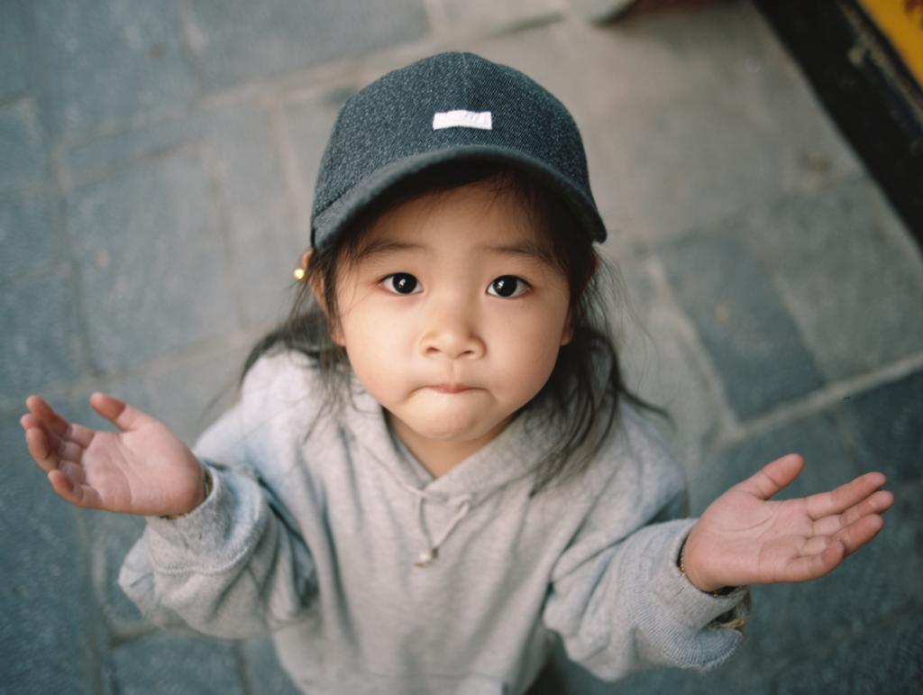 A young child holding their hands open in a gesture of curiosity and uncertainty, representing the natural process of asking questions and learning