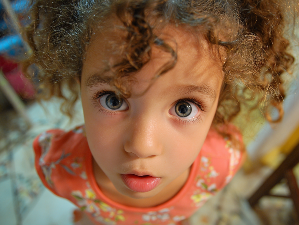 A young child looking up with wide eyes, expressing curiosity and attentiveness during a moment of questioning and discovery